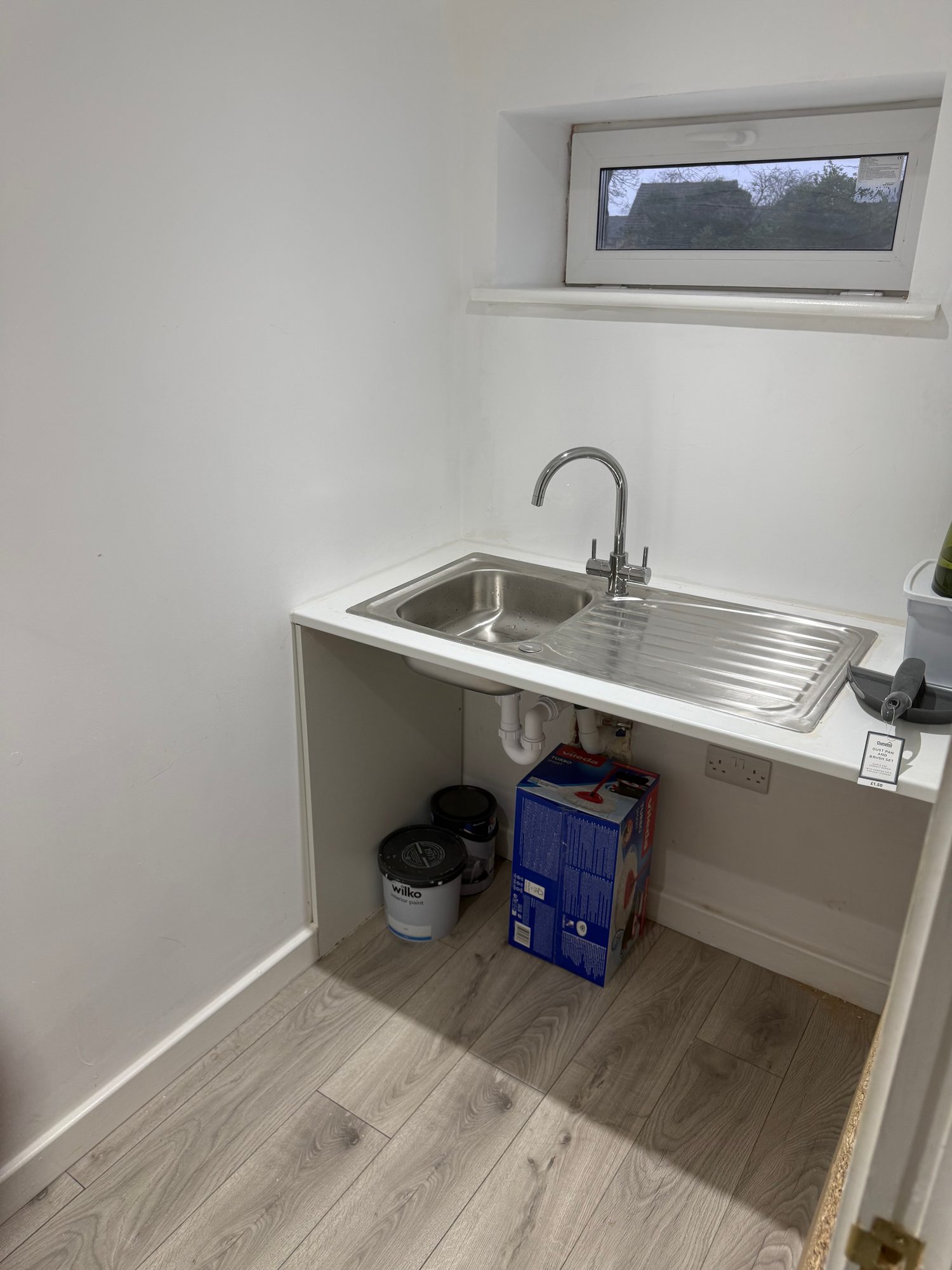 Finished utility area with a stainless steel sink and drainer, chrome tap, white walls, light wood-effect flooring and a small window