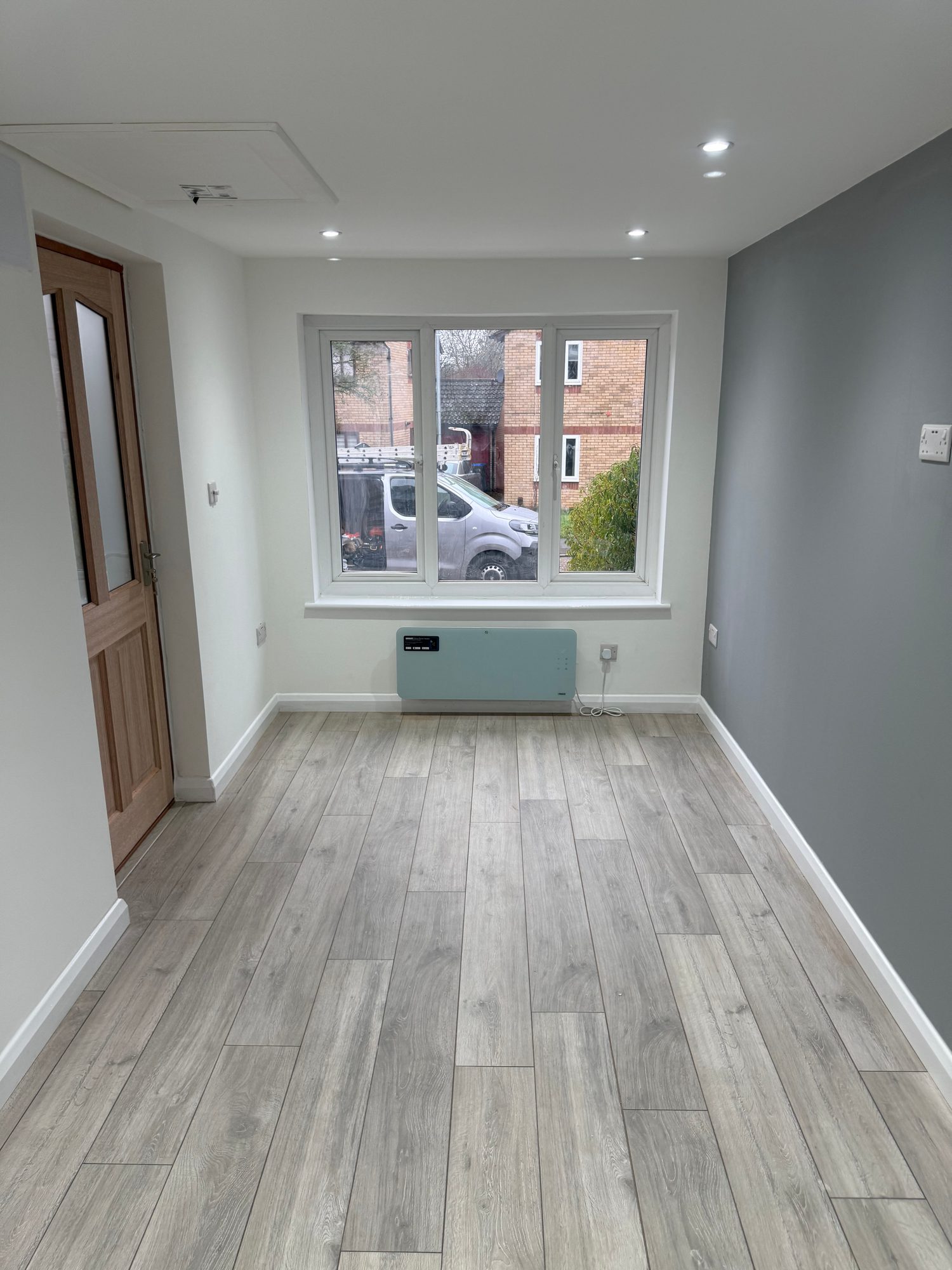 Finished interior room with wood-effect flooring, painted walls and ceiling, recessed spotlights, a three-section window, skirting boards and a wall-mounted heater