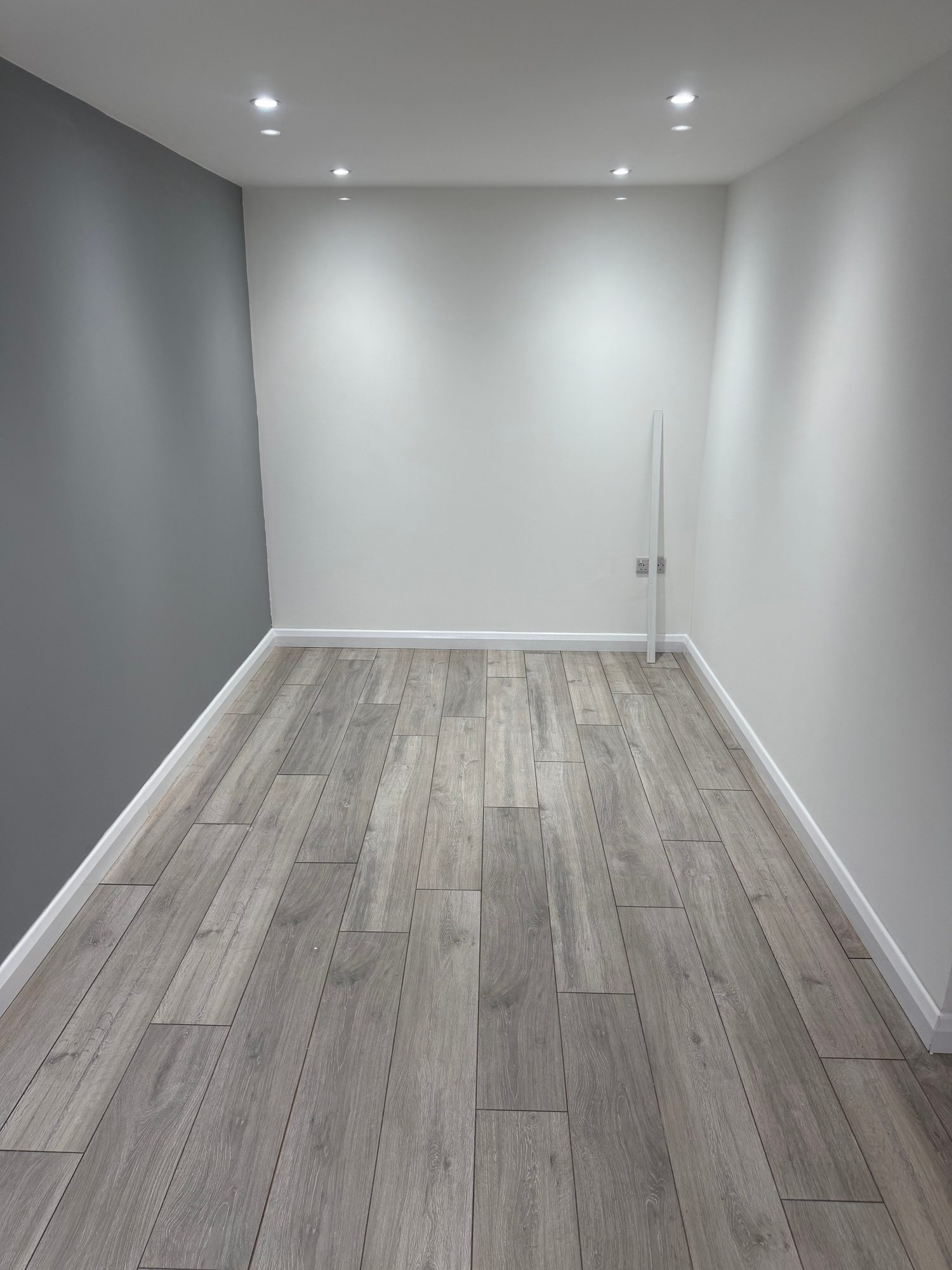 Finished room with grey wood-effect flooring, white and grey painted walls, white skirting boards and multiple recessed ceiling lights
