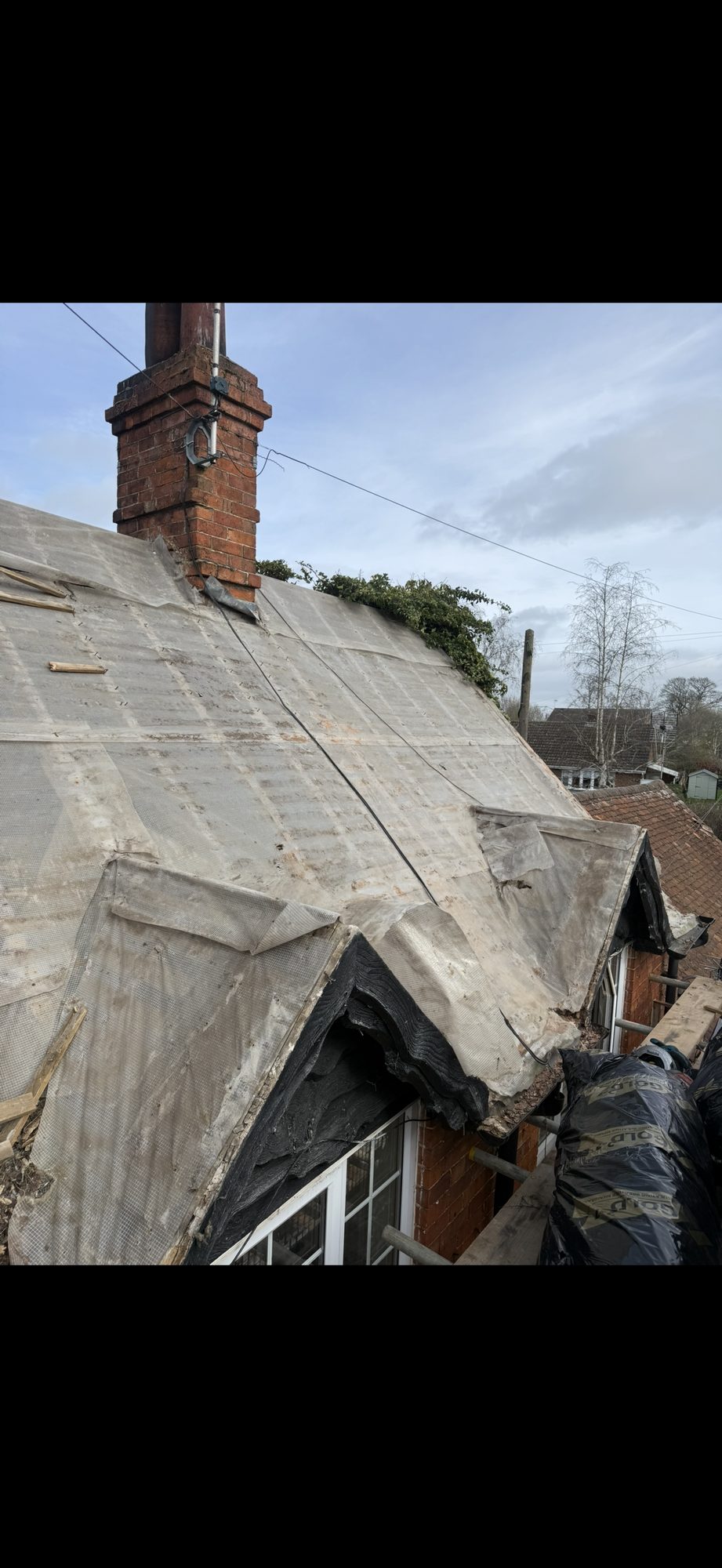 Main roof stripped of tiles, exposing the original underlay around the chimney and projecting window gables