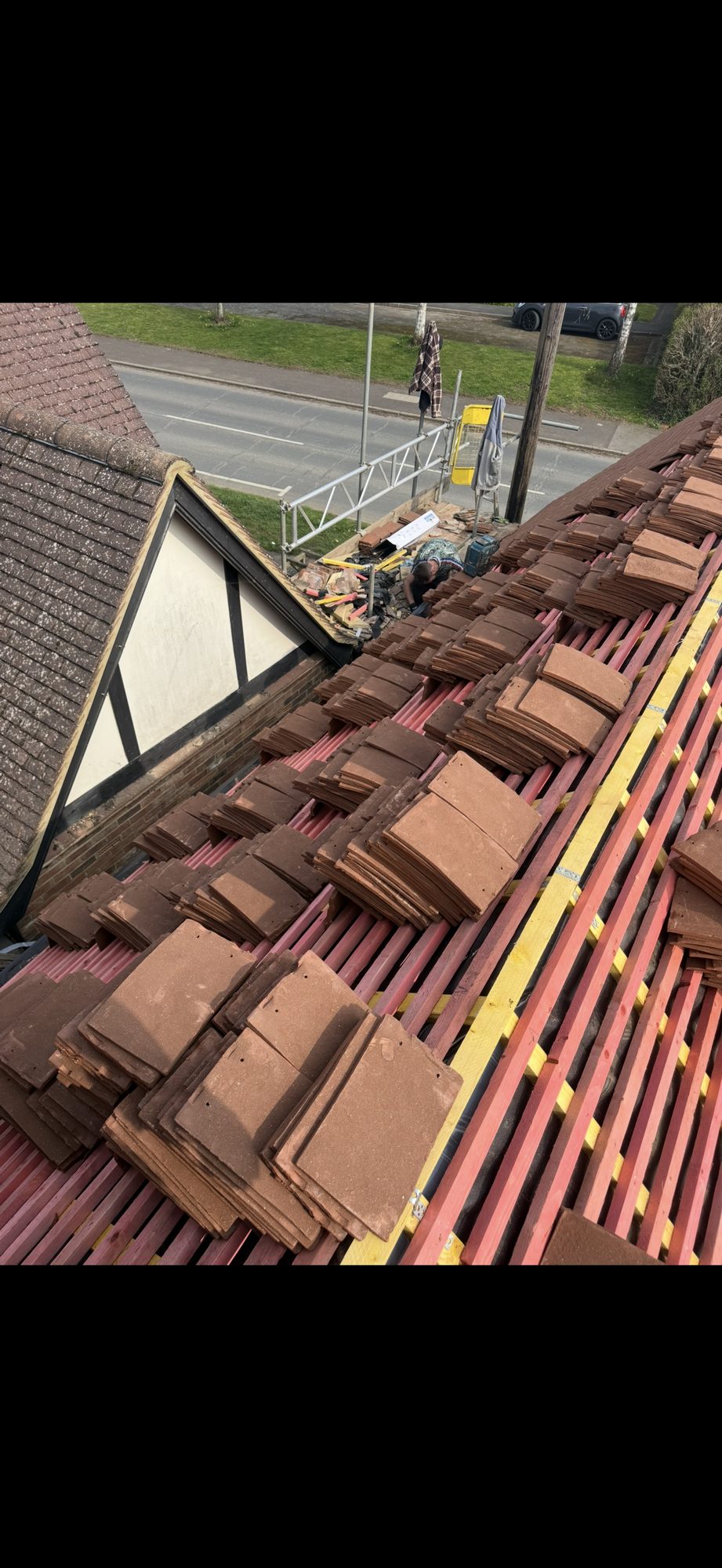 Stacks of roof tiles positioned across the battens with a worker continuing installation beside the scaffolding