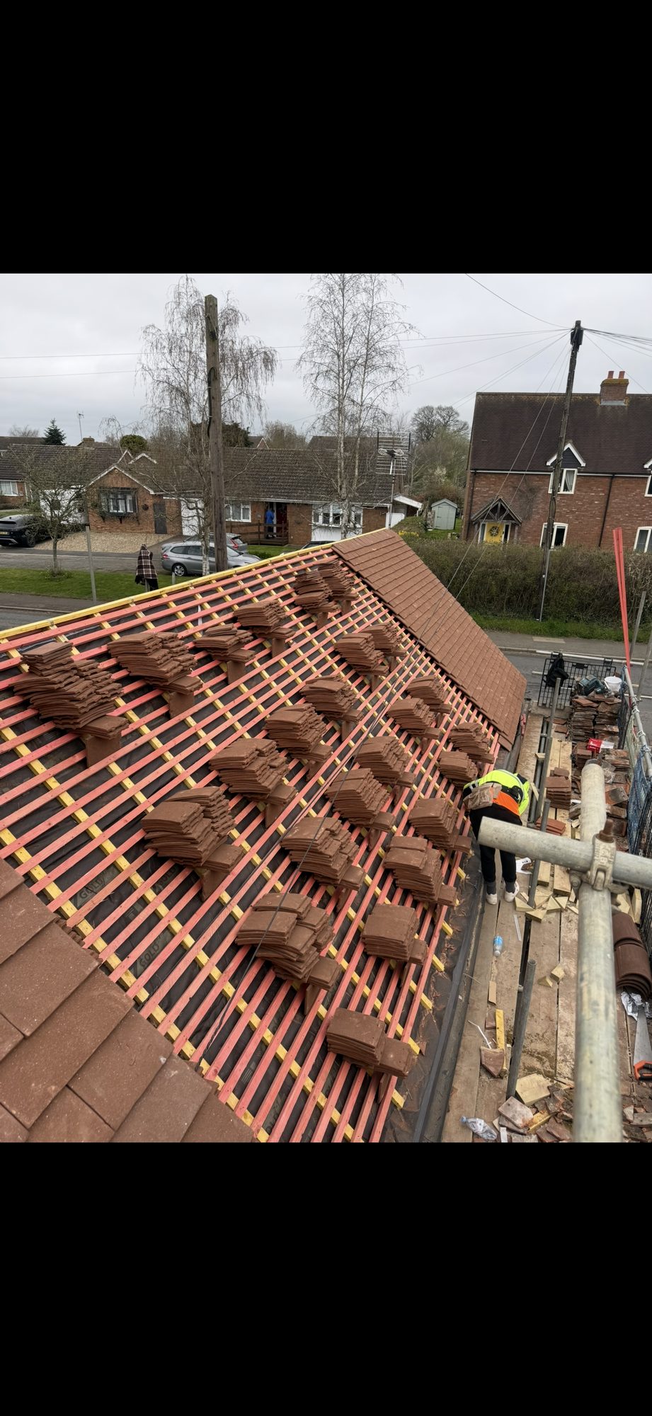 New tiles laid across one section of the roof while the remaining tiles are distributed over the exposed battens