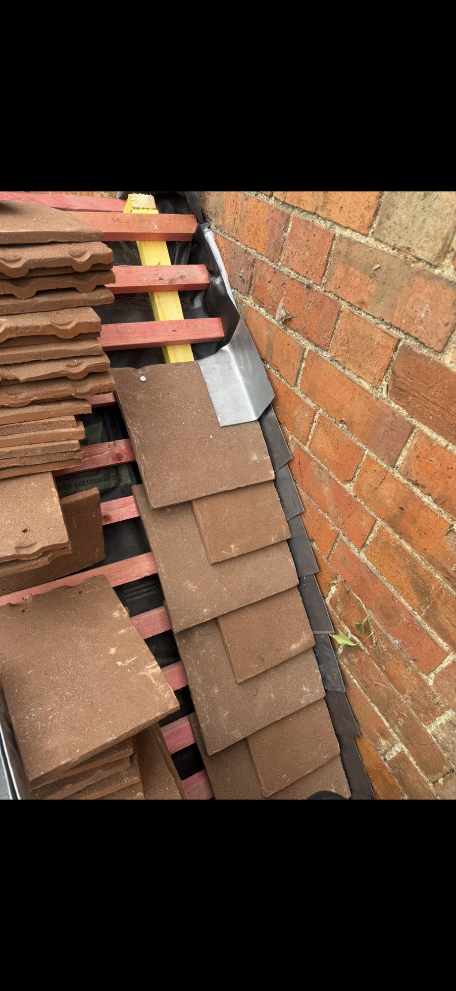 Stepped lead flashing fitted where the partially tiled roof meets the adjoining brick wall