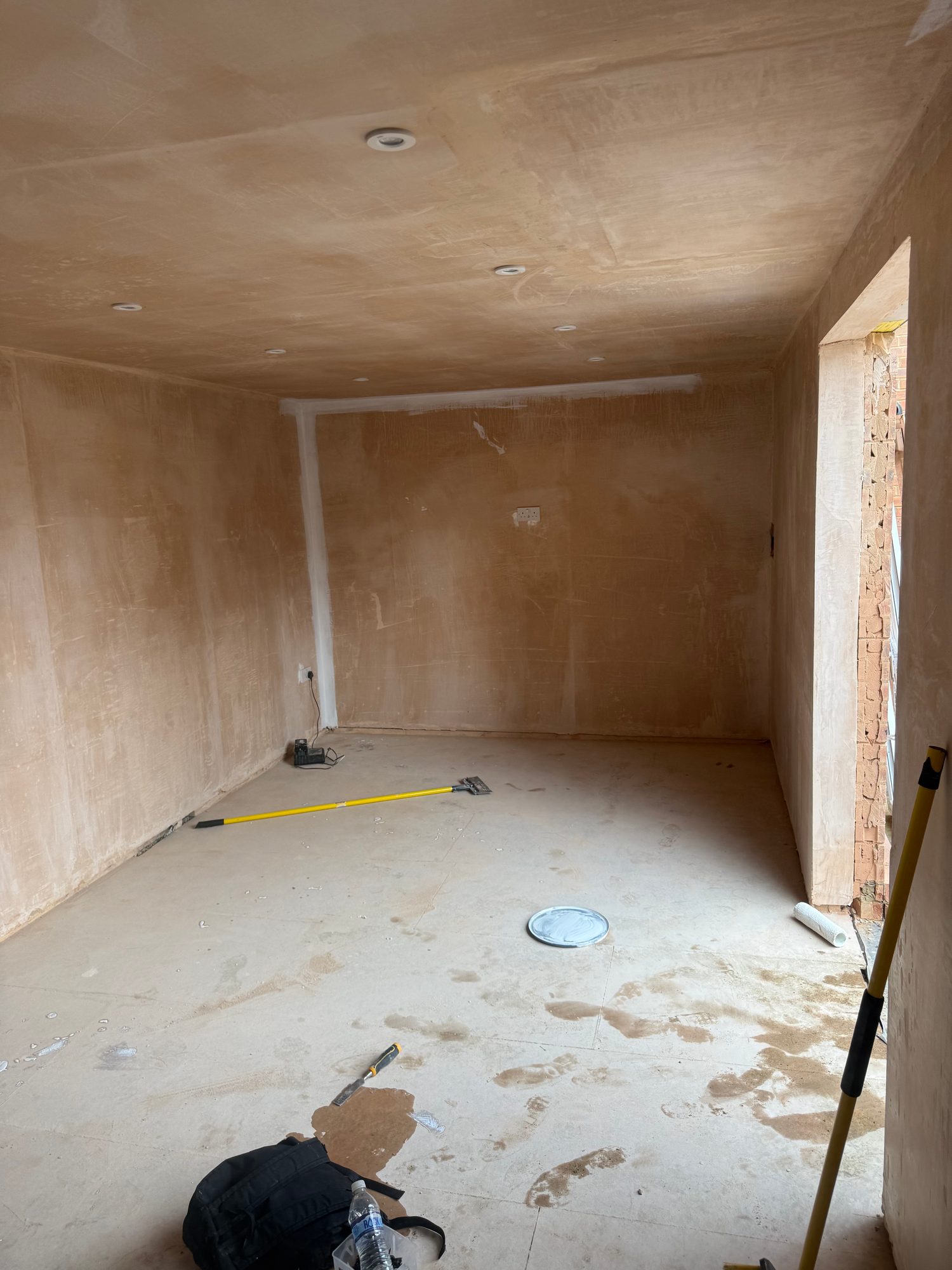 Interior during construction with newly plastered walls and ceiling, recessed light fittings and an unfinished floor