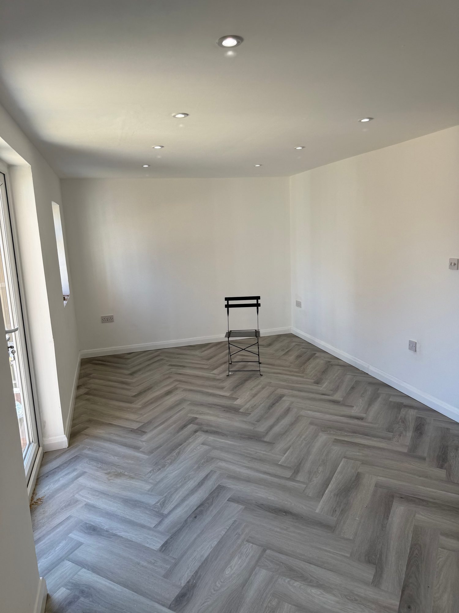 Wide view across the converted room with herringbone flooring and recessed lighting installed throughout
