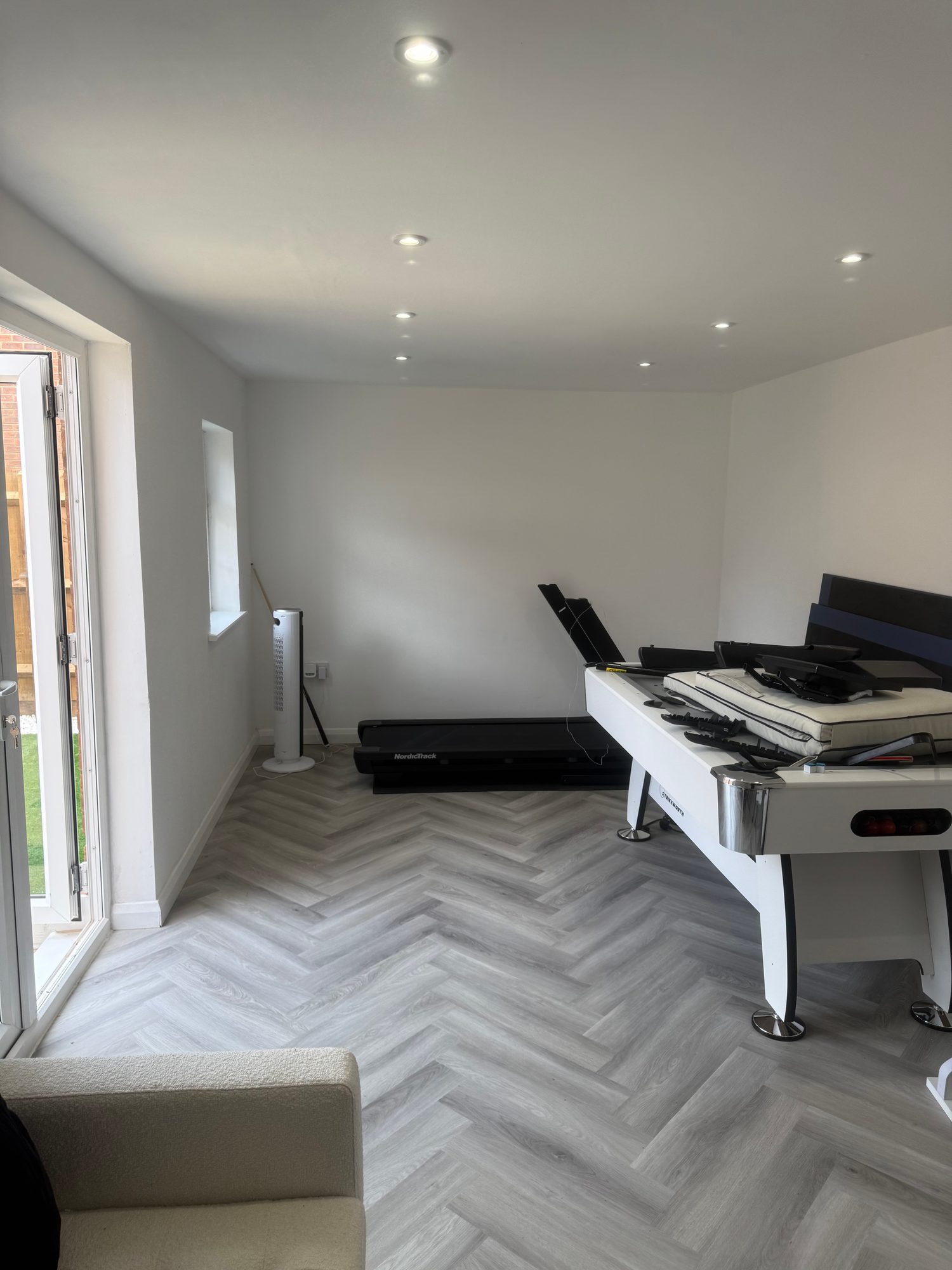Completed multi-purpose room with herringbone flooring, recessed lighting and space for games and exercise equipment