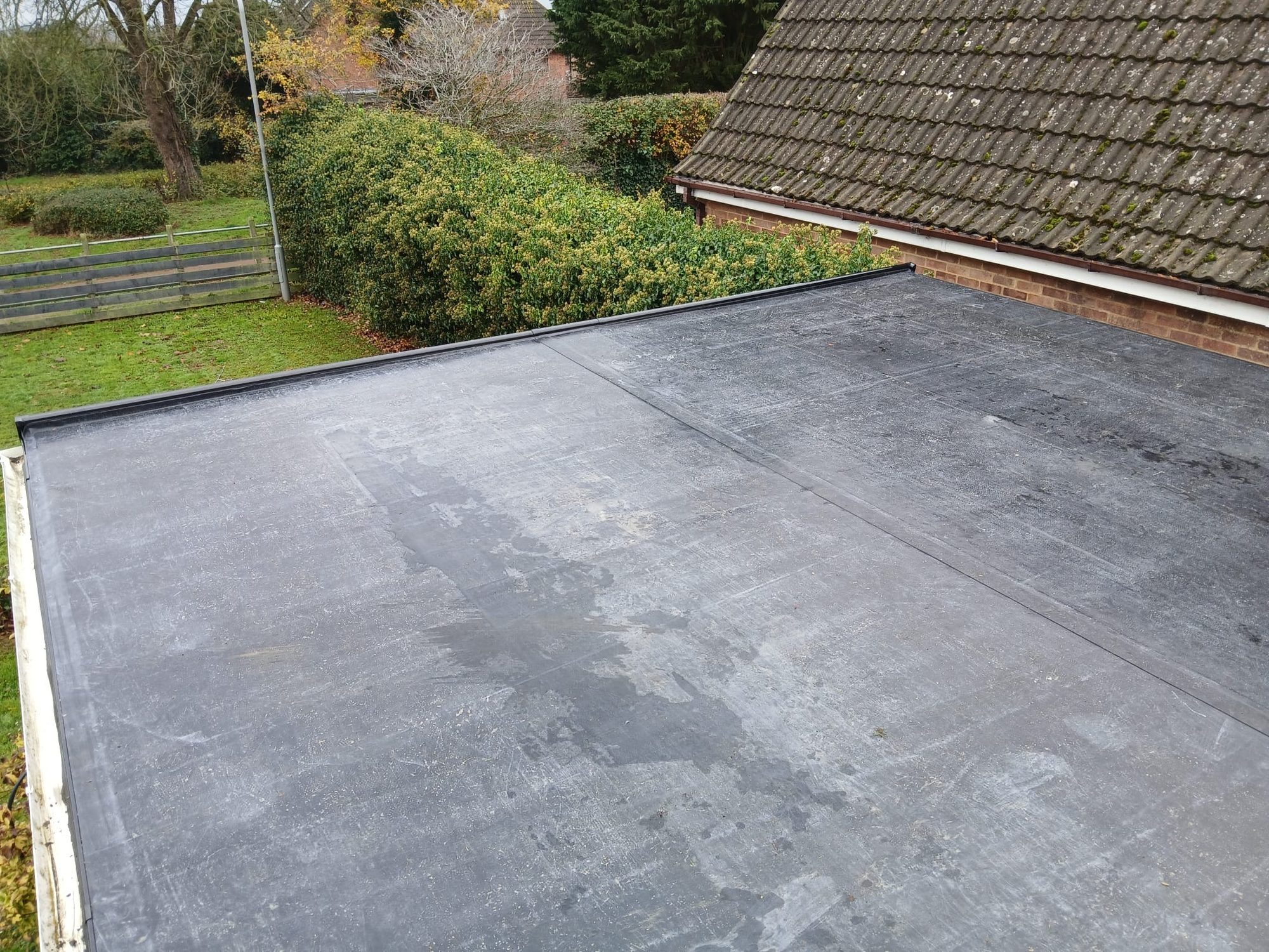 Wide view across a completed flat roof with a dark waterproof covering, visible sealed joints and raised edge trims