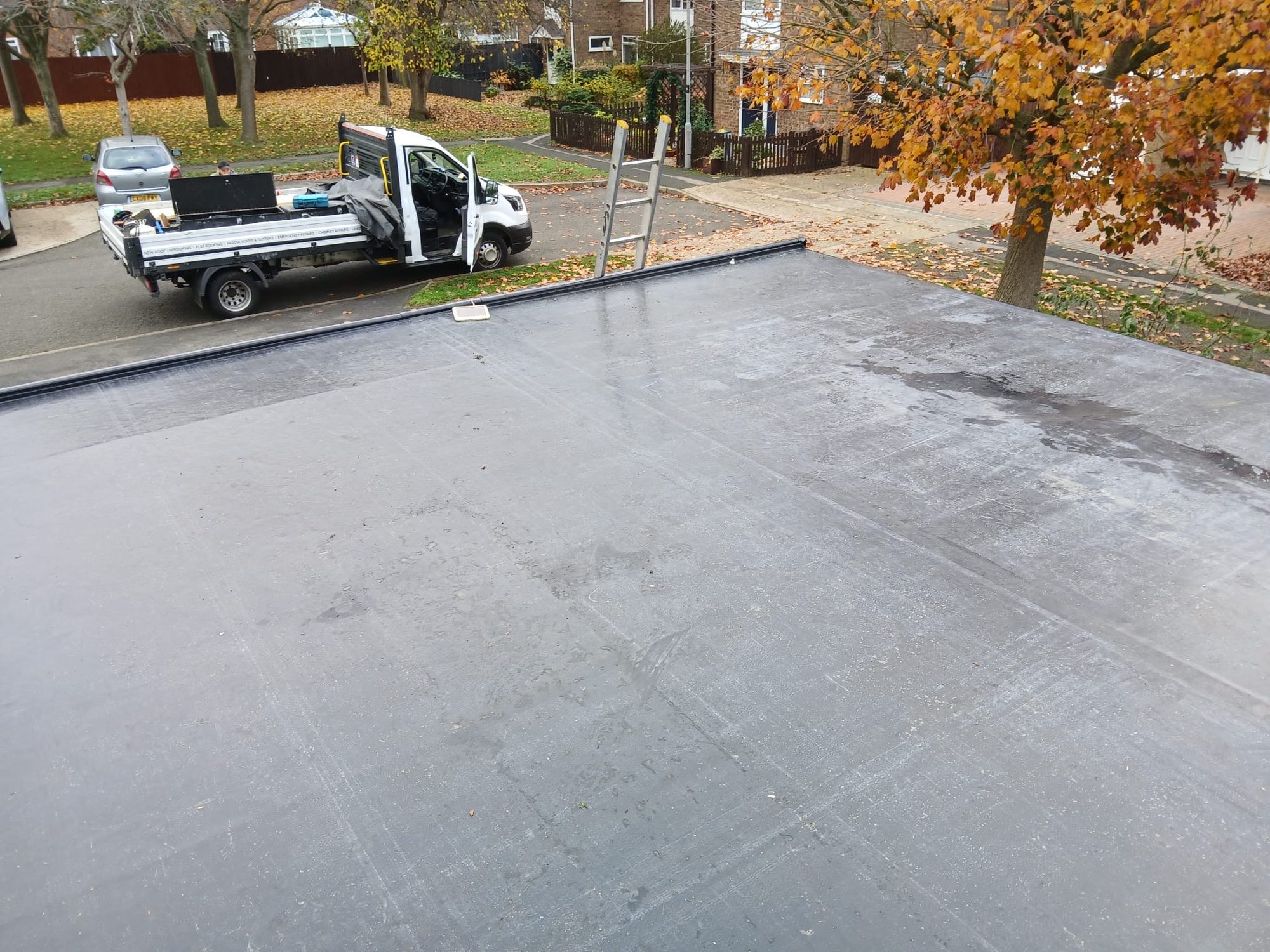 Completed dark flat roof membrane with raised perimeter trims and a work vehicle parked on the street below