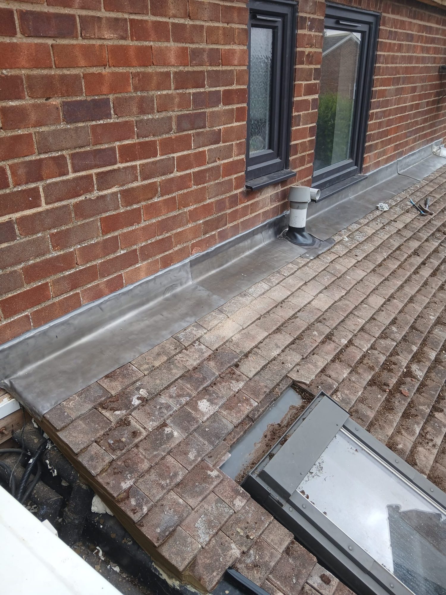 Lead flashing fitted where the tiled roof meets the brick wall with a roof window visible below