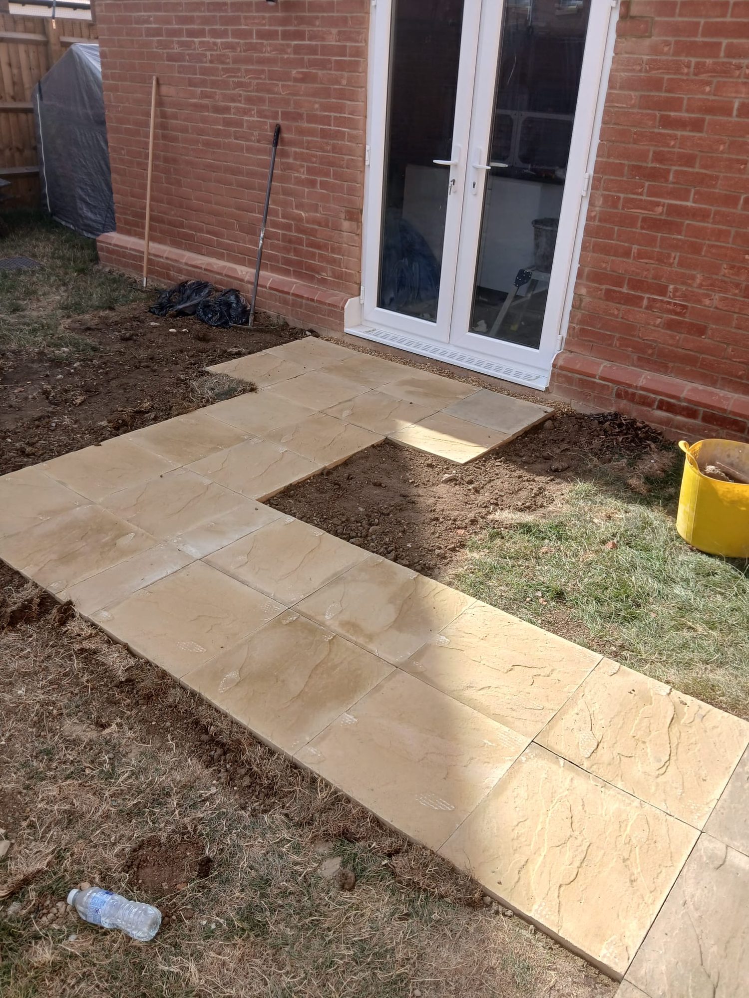 Buff-coloured paving slabs forming a path and seating area outside white-framed garden doors