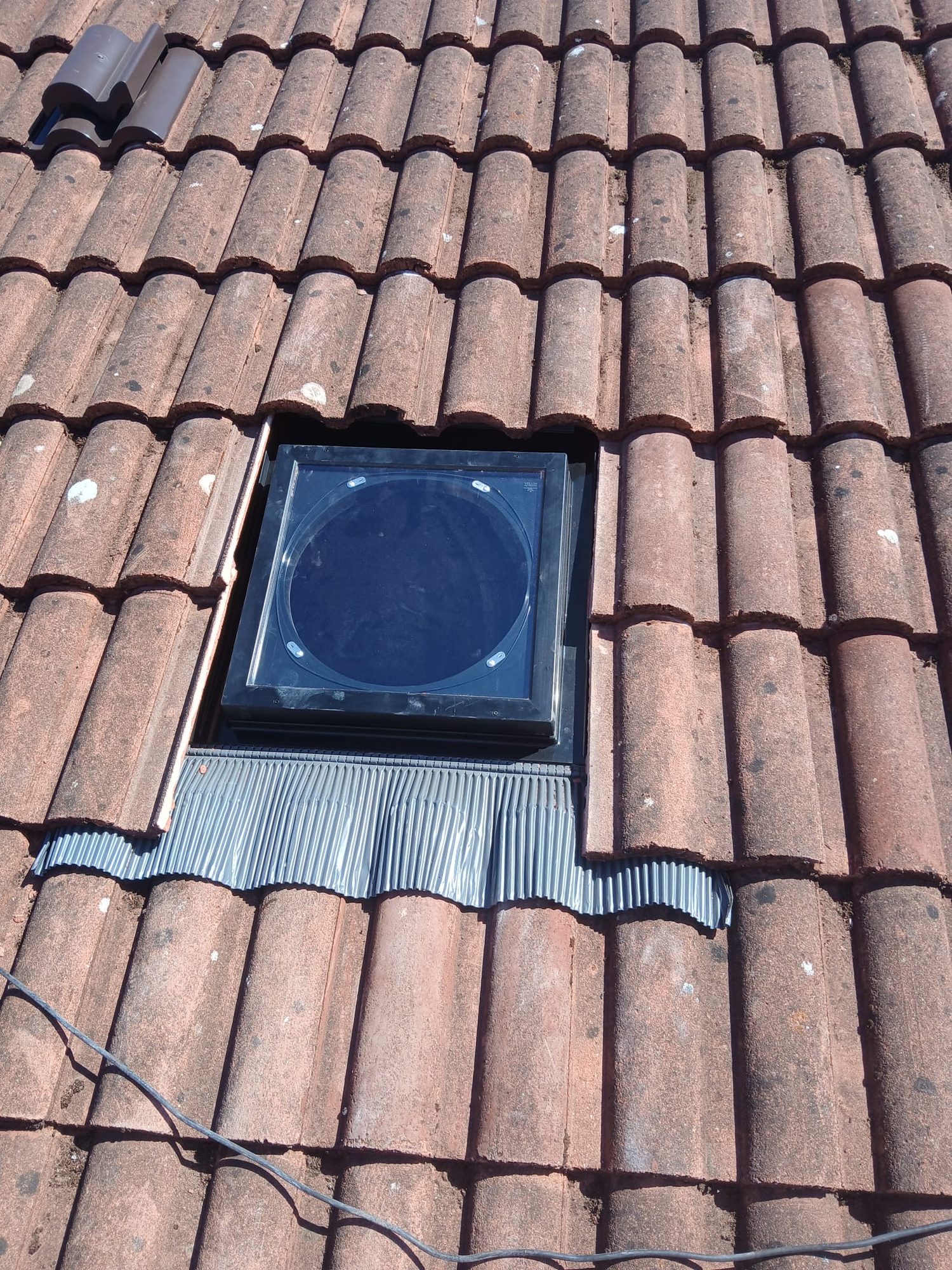 Grey-framed roof window installed among brown roof tiles with metal flashing fitted around the lower edge
