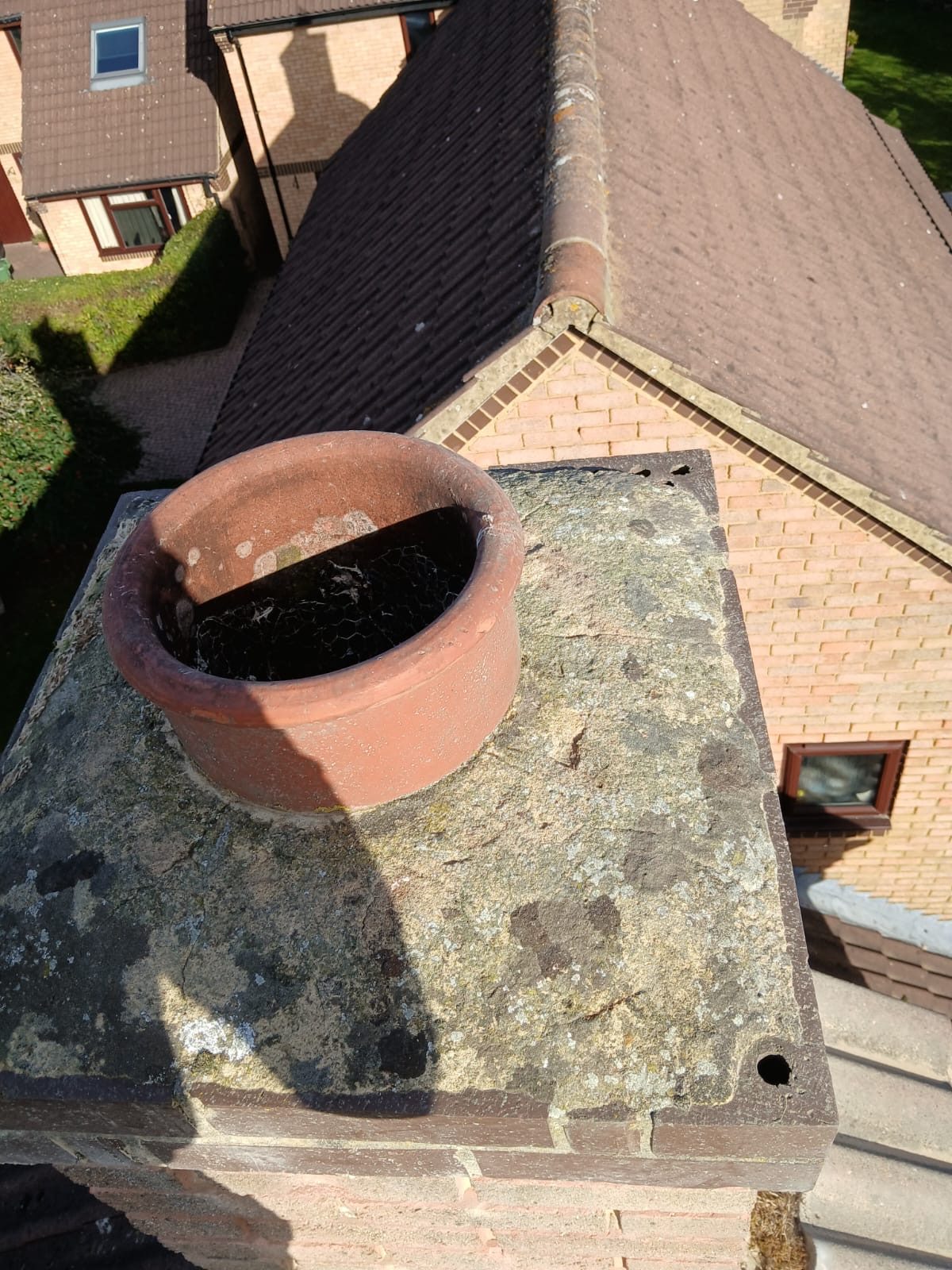 Weathered chimney top with a terracotta chimney pot, stained surface and visible holes around the edges