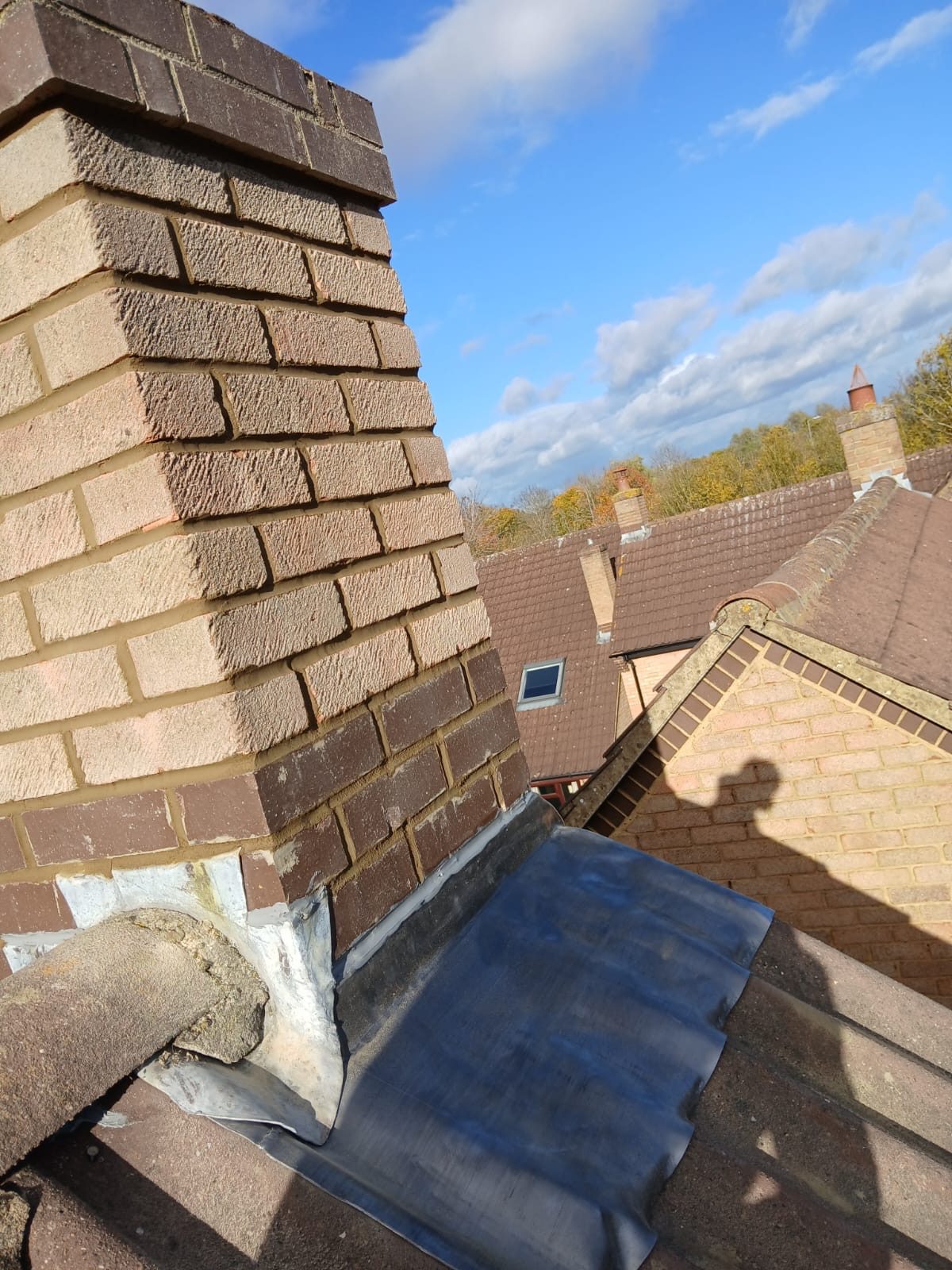 Side view of the rebuilt brick chimney with new lead flashing fitted around its base on the tiled roof