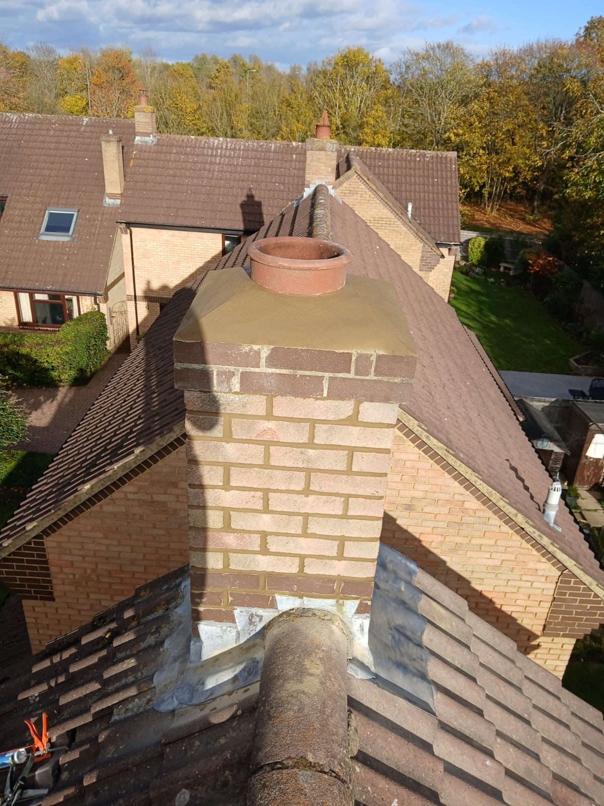 Full view of the rebuilt chimney with fresh brickwork, mortar cap, chimney pot and lead flashing