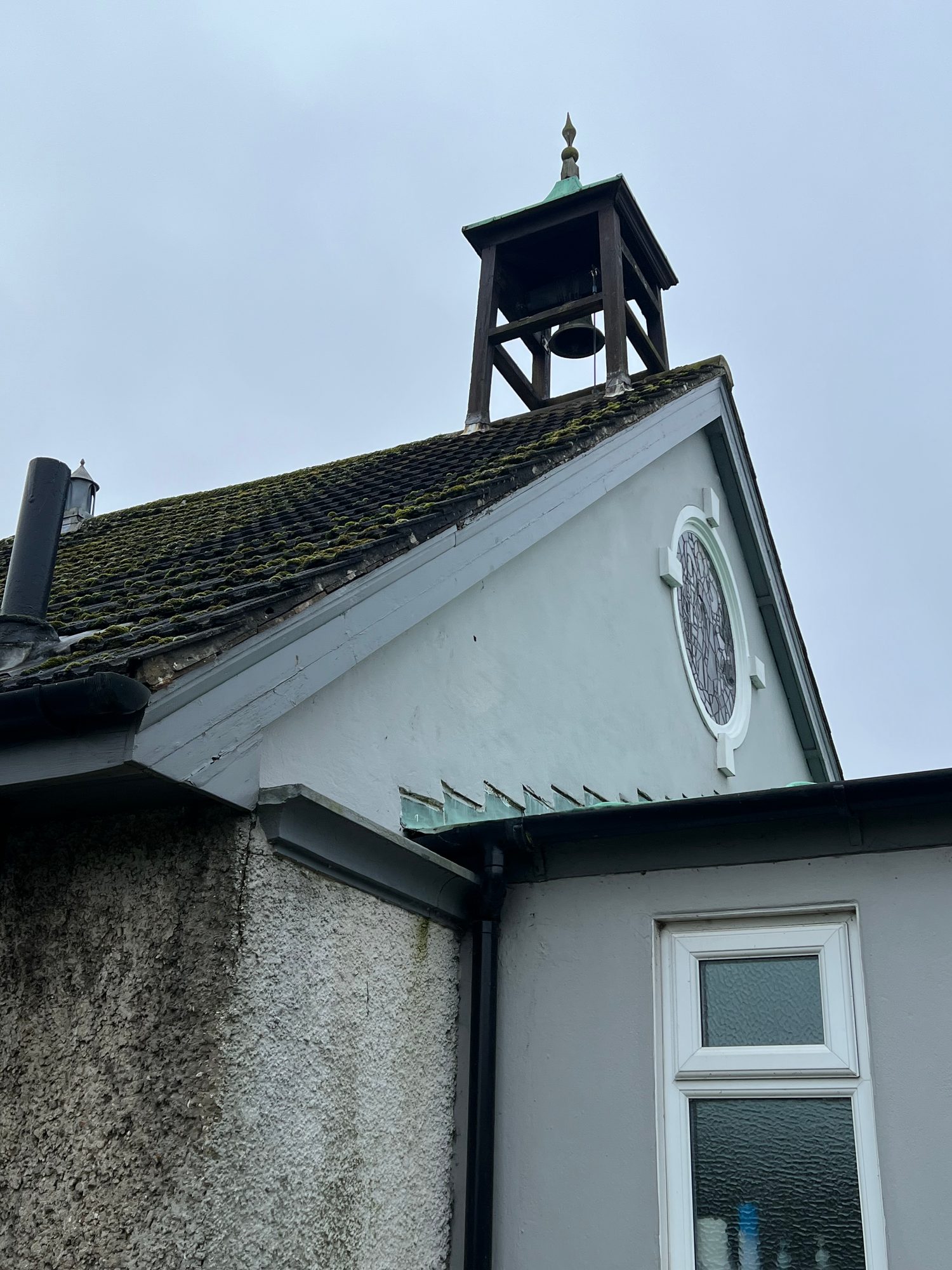 Small bell tower above a moss-covered pitched roof, with a white rendered gable and circular window below