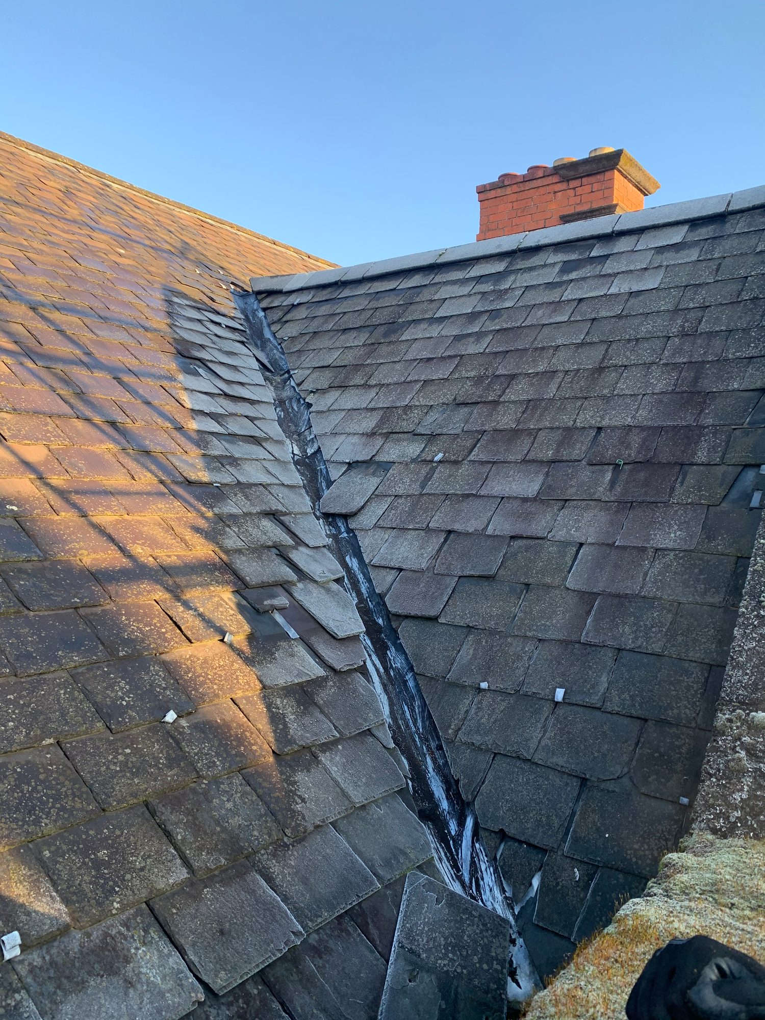 Before - The existing slate roof showing weathered and uneven slates around the roof valley before replacement works