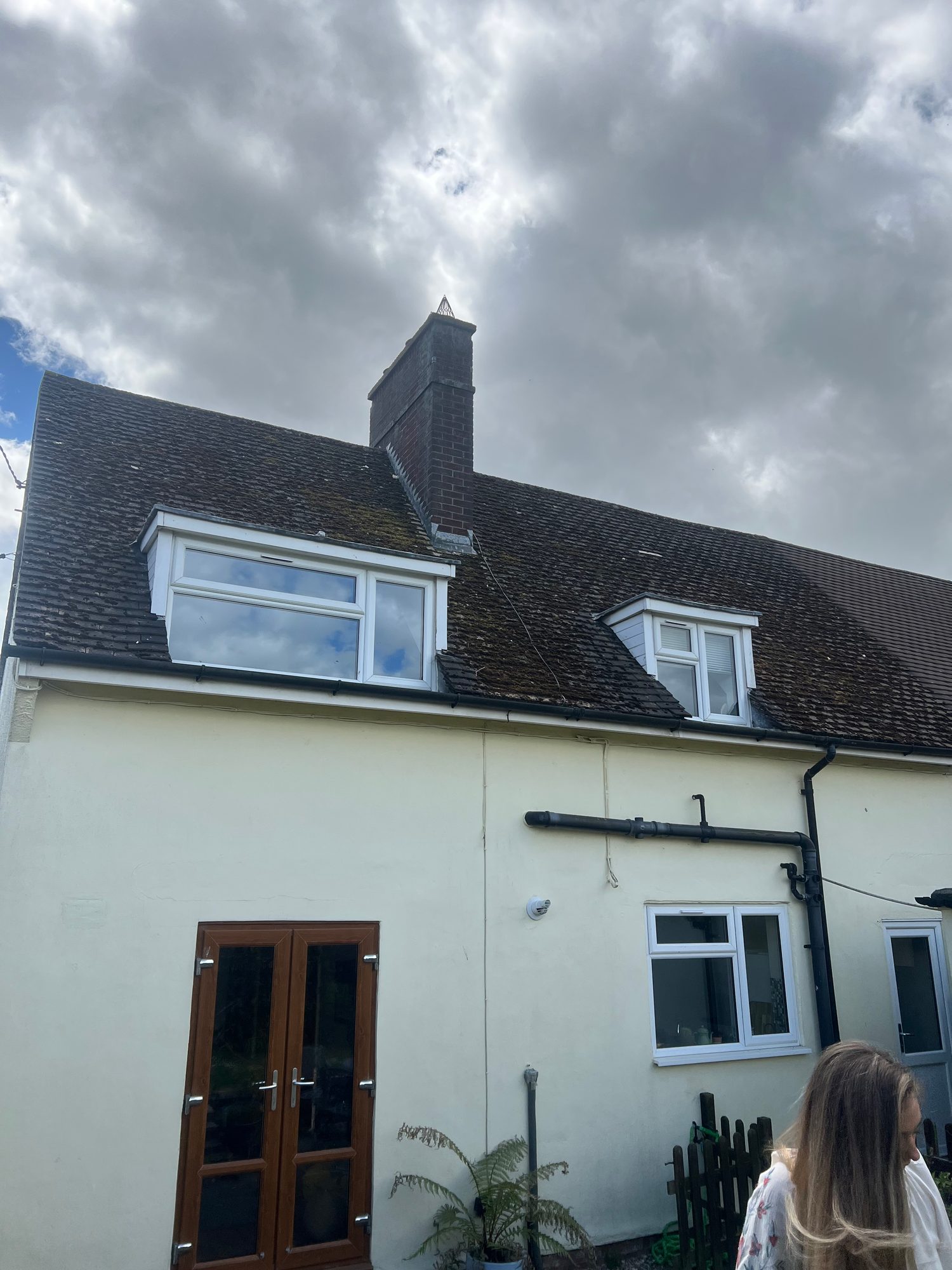 Moss and surface growth covering the roof tiles around the chimney and dormer windows
