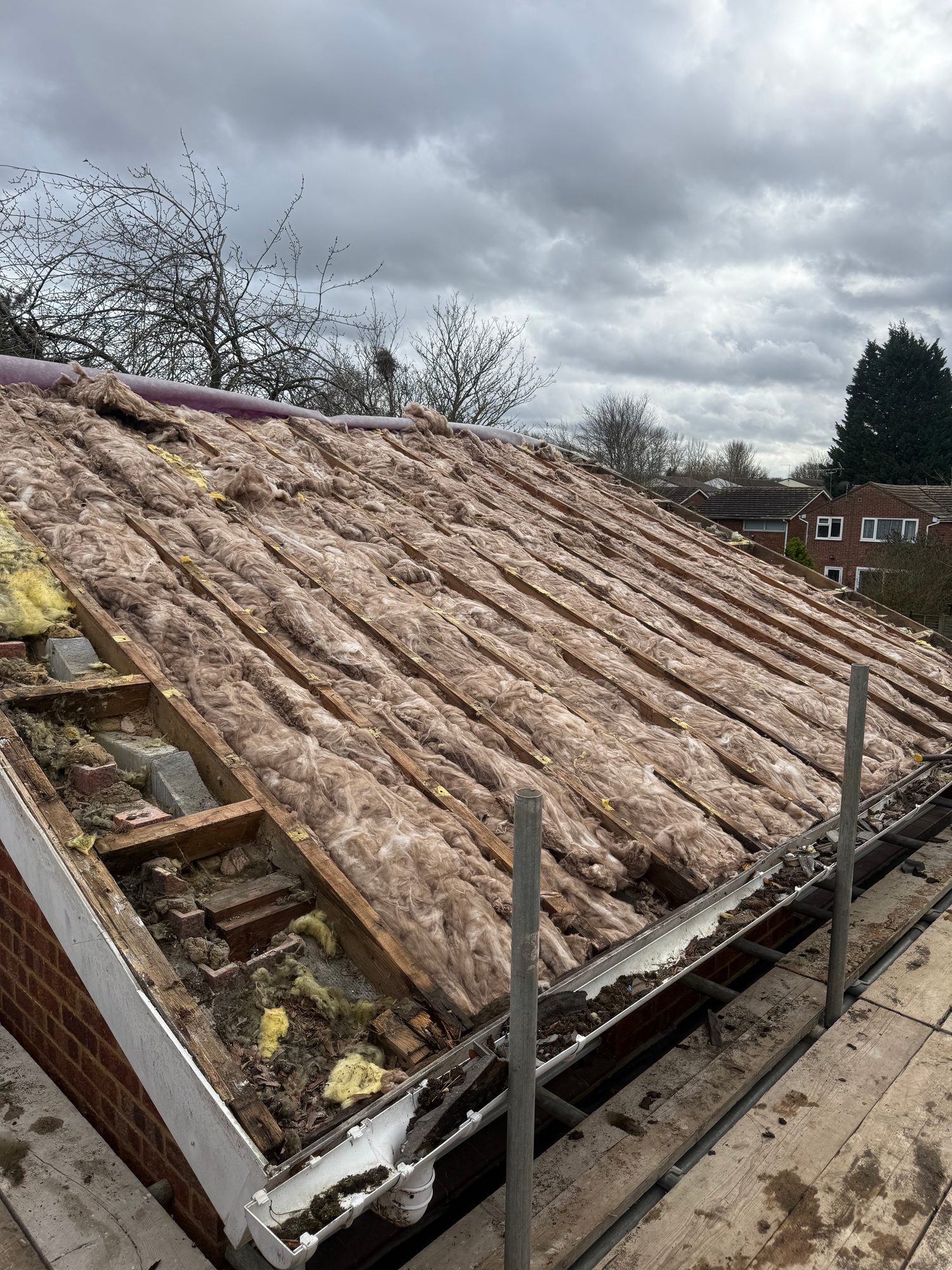 Pitched roof with mineral wool insulation fitted between timber rafters, with the roof edge, guttering and scaffolding visible