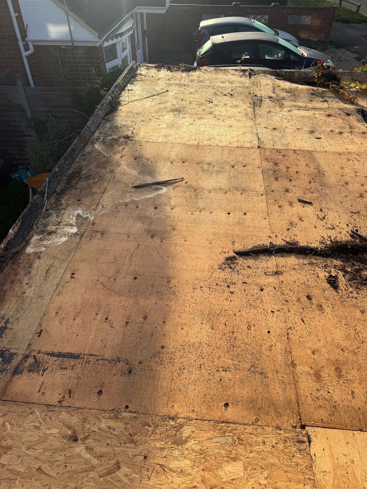 View across a flat roof with exposed timber decking, roof edges visible around the perimeter and debris from ongoing work on the surface