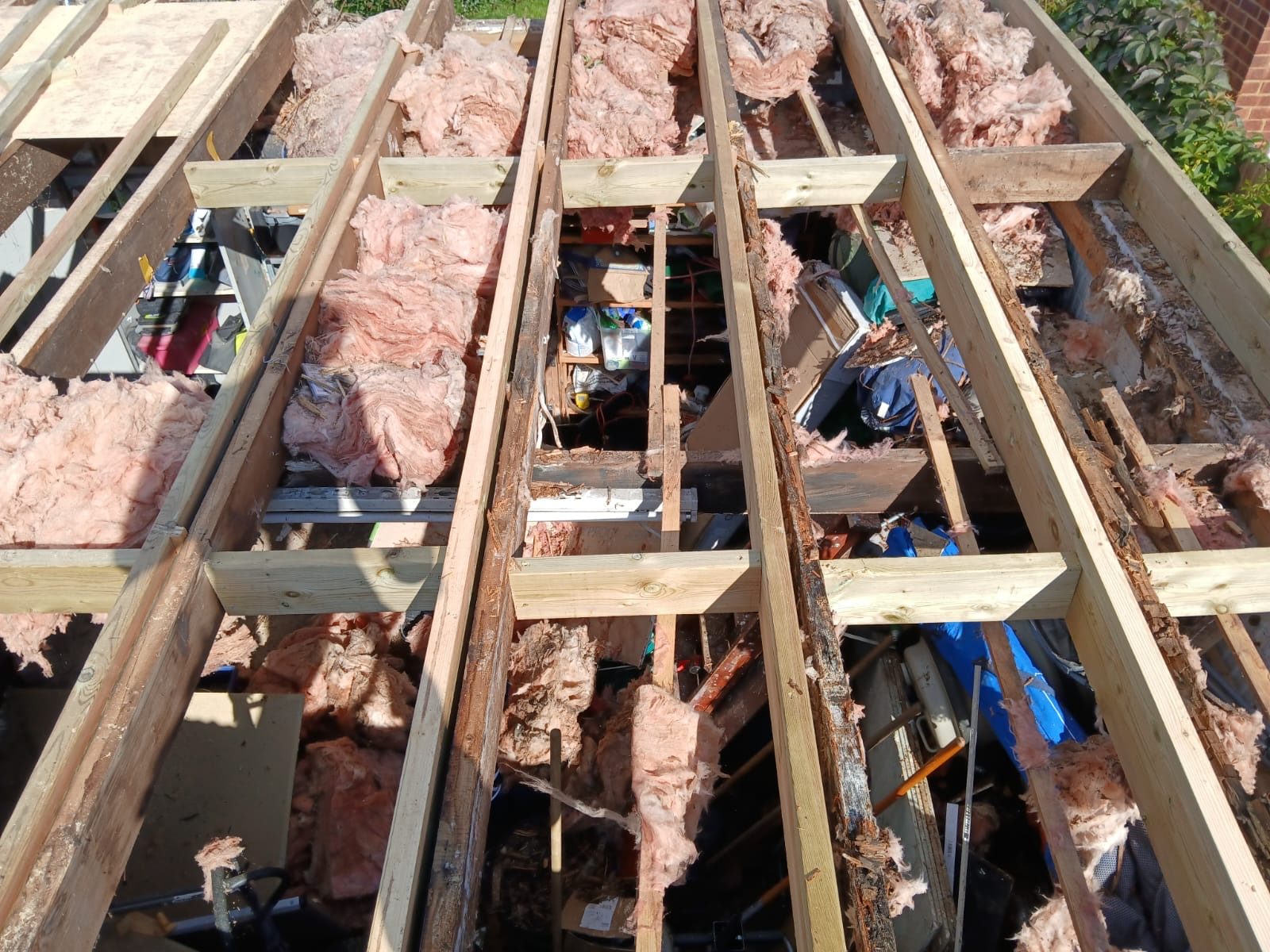 Exposed timber roof joists with sections of pink insulation fitted between them, with construction materials and tools visible below