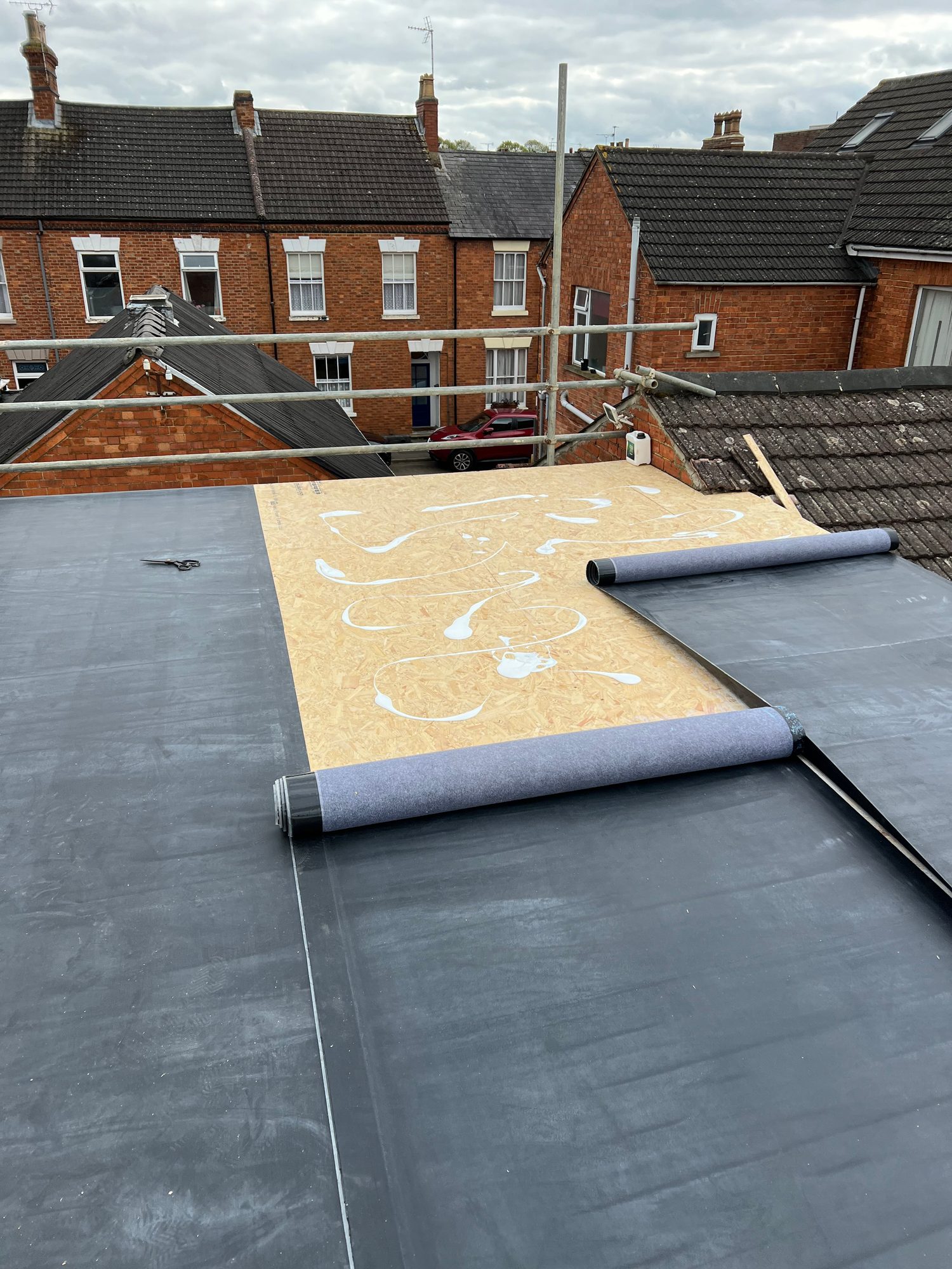 During - The flat roof during installation with sections of the roofing membrane being laid over the timber decking