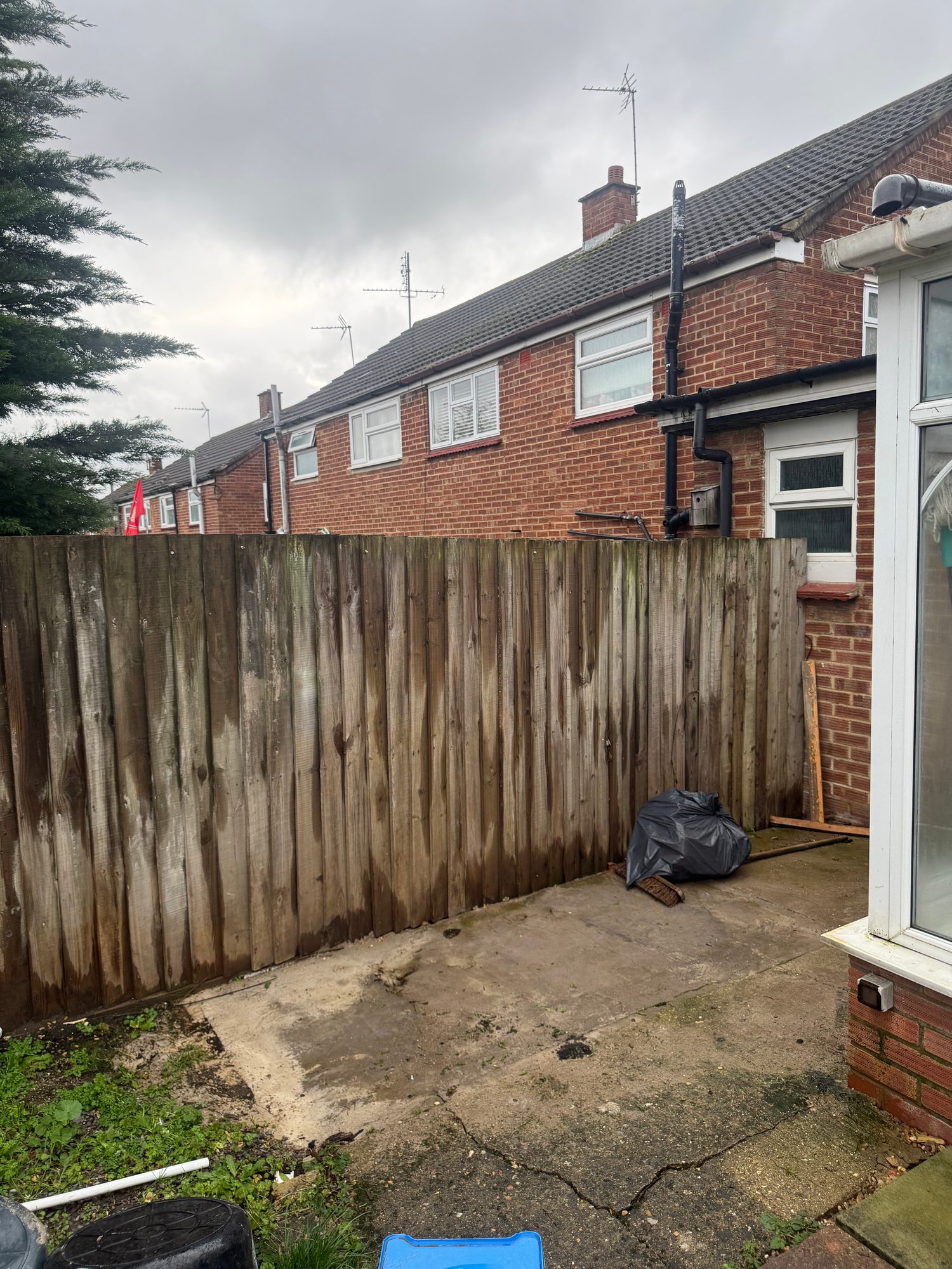 Tall weathered timber fence panels beside a cracked paved area at the rear of the property
