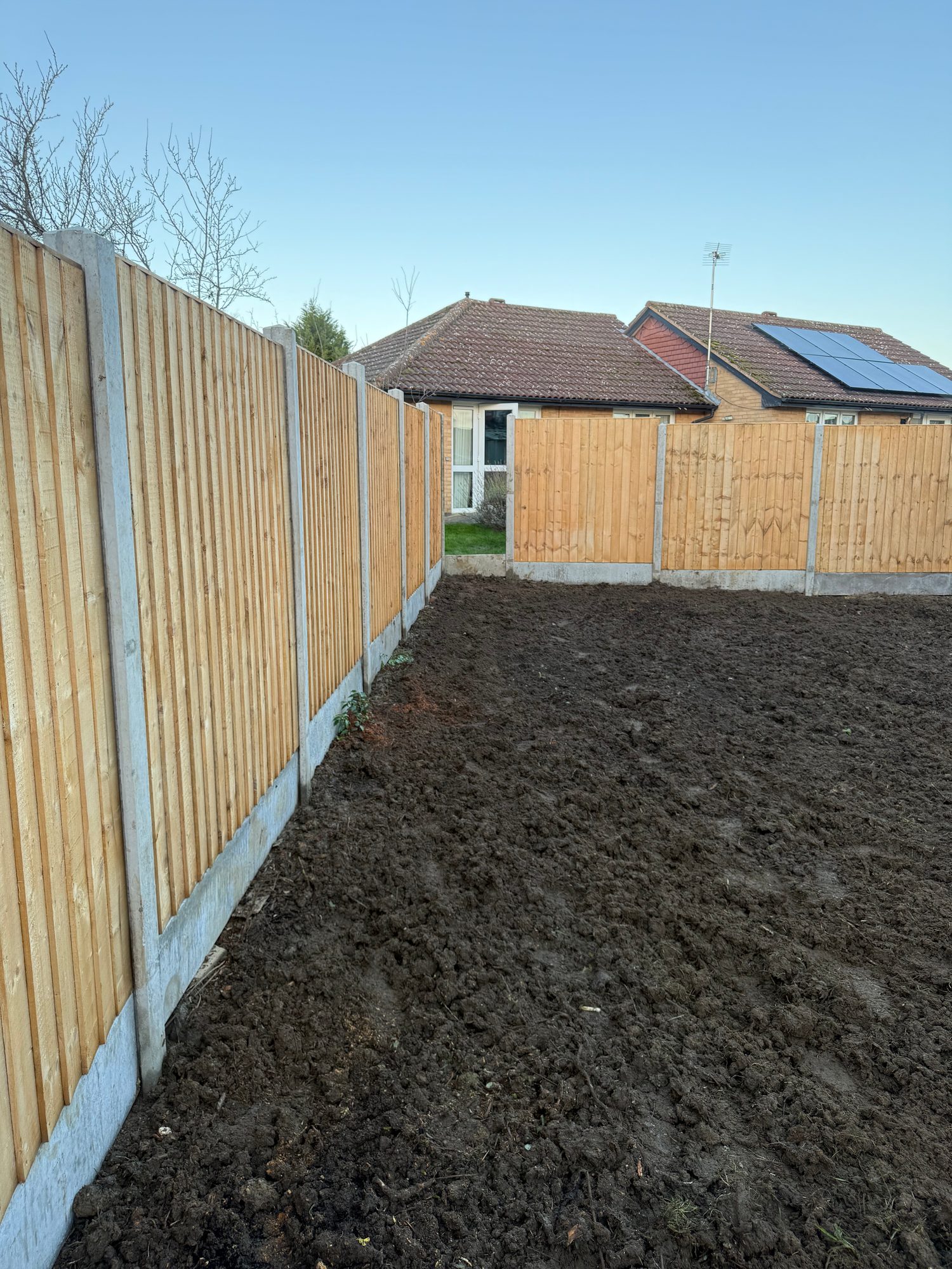 Newly installed timber fence panels with concrete posts surrounding cleared and prepared garden soil