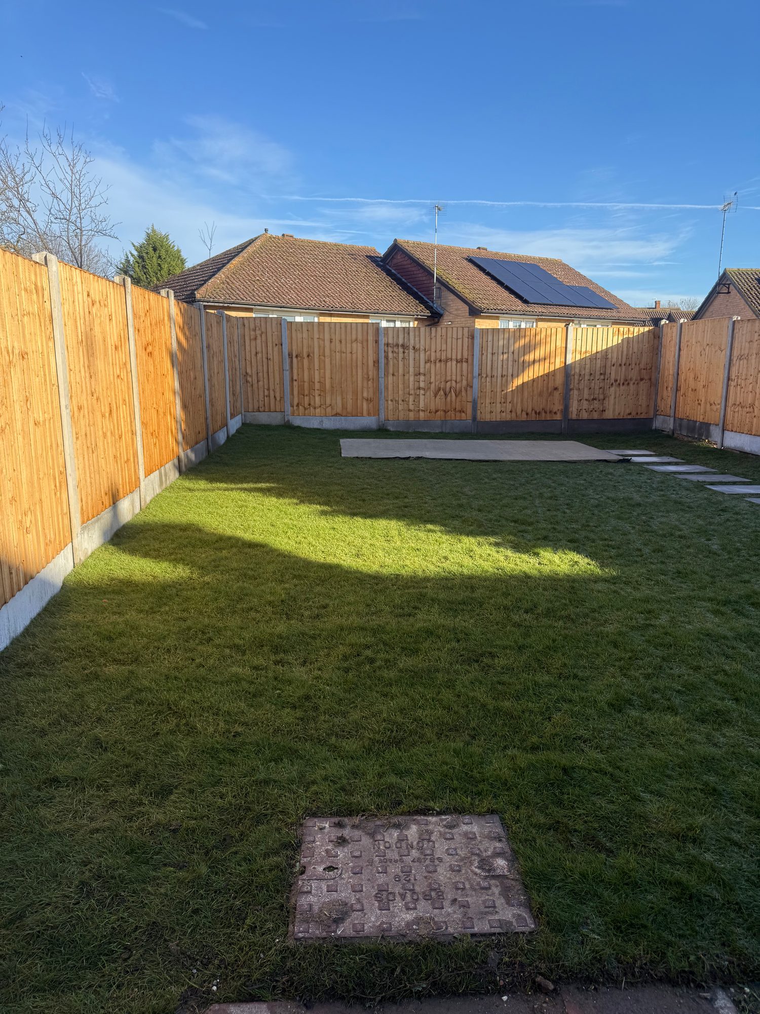 Wide view of the completed garden with fresh turf, new timber fencing and a rectangular base